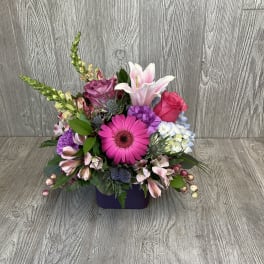 Mixed bouquet in a purple container with pink, white, and purple blooms