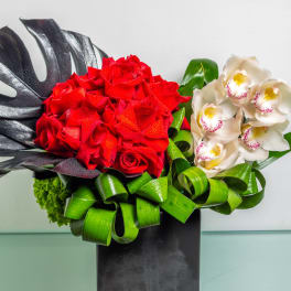 Red roses and white orchids in a black vase with green ribbon loops