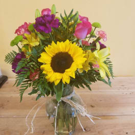 Mixed bouquet with a sunflower, pink roses, and purple flowers in a glass vase