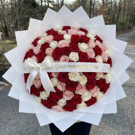 Large bouquet of red, pink, and white roses wrapped in white paper with a ribbon