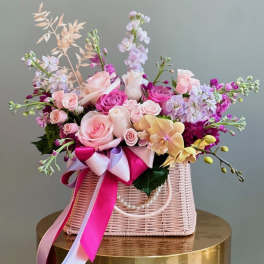 Pink and lavender floral arrangement in a woven basket with ribbon