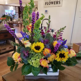 Bright mixed arrangement with sunflowers, roses, and purple flowers in a white wooden box.