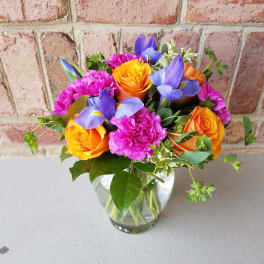 Small clear vase with orange roses, purple iris, and bright pink carnations