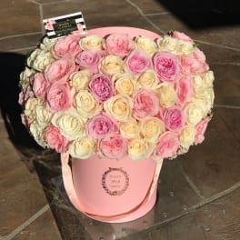 Pink and cream roses arranged in a round pink hat box