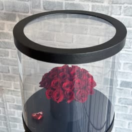 Red roses arranged in a black round box with a clear lid
