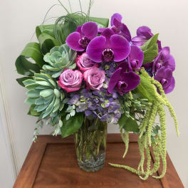 Purple orchids and pink roses in a glass vase with succulents