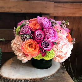 Bouquet of pink, peach, and lavender roses with hydrangeas in a black vase
