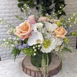 Mixed bouquet with peach roses, white orchids, and pastel flowers in a green vase
