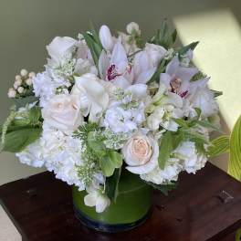 White floral arrangement with roses, orchids, and calla lilies in a green vase