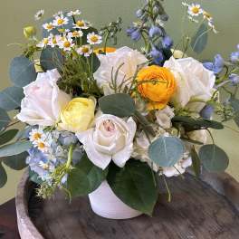 Mixed bouquet of white roses, yellow ranunculus, and blue flowers in a white vase