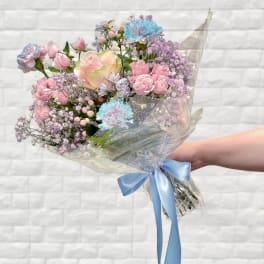 Handheld bouquet of pink and blue flowers wrapped in clear plastic with a blue ribbon