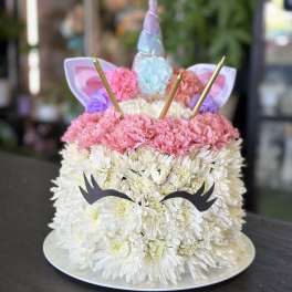 Unicorn-shaped floral cake with white and pink flowers on a round tray
