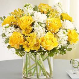 Yellow roses and white flowers arranged in a clear glass vase