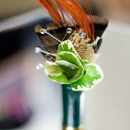 Decorative boutonniere with orange feathers and green variegated leaves