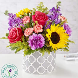 Mixed bouquet with roses, sunflowers, and purple blooms in a white vase