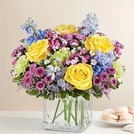 Yellow roses and pastel mixed flowers in a clear square vase