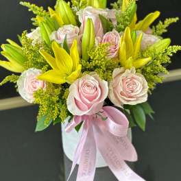 Pink roses and yellow lilies arranged in a white box with a pink ribbon