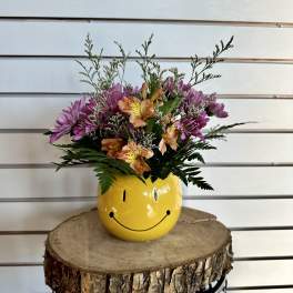 Bouquet of purple and orange flowers in a yellow smiley-face vase