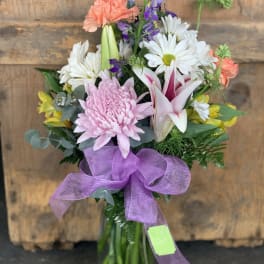 Mixed bouquet with pink, white, purple, and yellow flowers in a glass vase