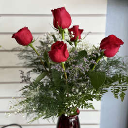Red roses arranged in a burgundy vase with airy filler flowers