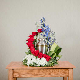 Red roses and blue flowers arranged around a silver urn on a table.