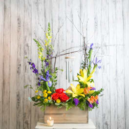 Colorful floral arrangement in a wooden box with a candle in front
