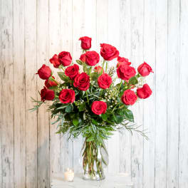 Red roses arranged in a clear glass vase with greenery