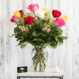 Mixed roses in a clear glass vase with a small candle beside it