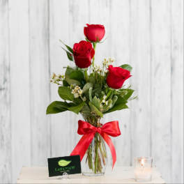 Three red roses in a clear vase with a red ribbon.