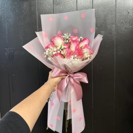 Pink rose bouquet wrapped in translucent polka-dot paper with a satin ribbon