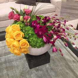 Mixed bouquet with yellow roses, pink lisianthus, and purple orchids in a white vase