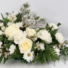 White floral arrangement with roses and daisies around an angel figurine