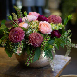 Low floral arrangement with pink and burgundy blooms in a metal bowl