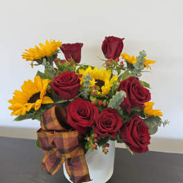 Arrangement of red roses and yellow sunflowers in a white container with a plaid bow.