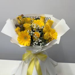 Yellow roses and gerbera daisies wrapped in white paper with a yellow ribbon