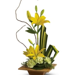 Yellow lilies arranged in a wooden vase with green accents