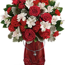 Red roses and white lilies in a red vase with a heart charm