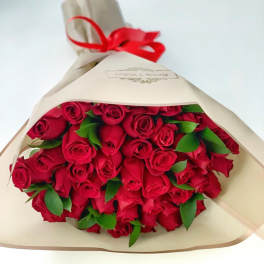 Large bouquet of red roses wrapped in cream paper and tied with a red ribbon
