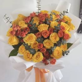 Bouquet of yellow and coral roses wrapped in white paper with an orange ribbon