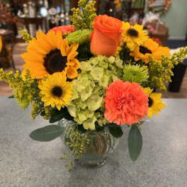Bright bouquet with sunflowers, orange roses, and carnations in a glass vase