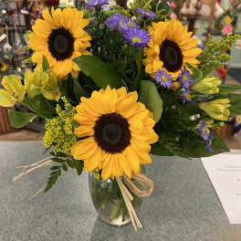 Bouquet of sunflowers, purple asters, and yellow lilies in a glass vase