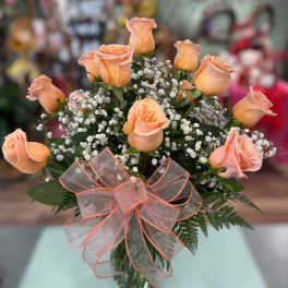 Peach roses in a glass vase with baby's breath and a sheer ribbon bow
