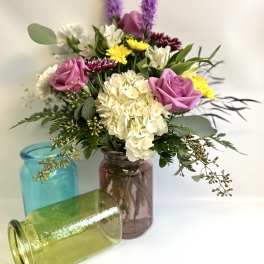 Mixed bouquet in colorful glass jars with pink roses and white hydrangea