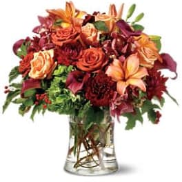 Mixed bouquet of orange, red, and peach flowers in a clear glass vase