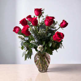 Red roses arranged in a clear glass vase with mixed greenery