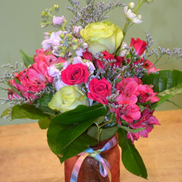 Bouquet of pink and green roses with purple filler in a glass jar
