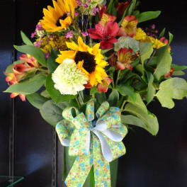 Tall mixed bouquet with sunflowers, lilies, and a decorative bow in a green vase