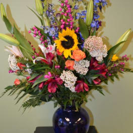 Colorful mixed bouquet in a blue glass vase with a sunflower and lilies