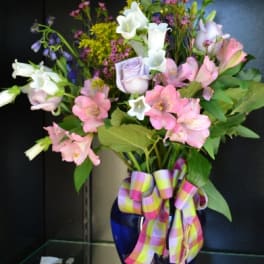 Mixed bouquet of pink, white, and lavender flowers in a blue vase with a plaid ribbon
