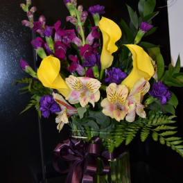 Bouquet of yellow calla lilies, purple flowers, and striped alstroemeria in a glass vase